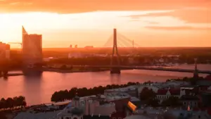 Panorāmas skats uz Rīgas pilsētu ar Vanšu tiltu saulrietā pār Daugavu.