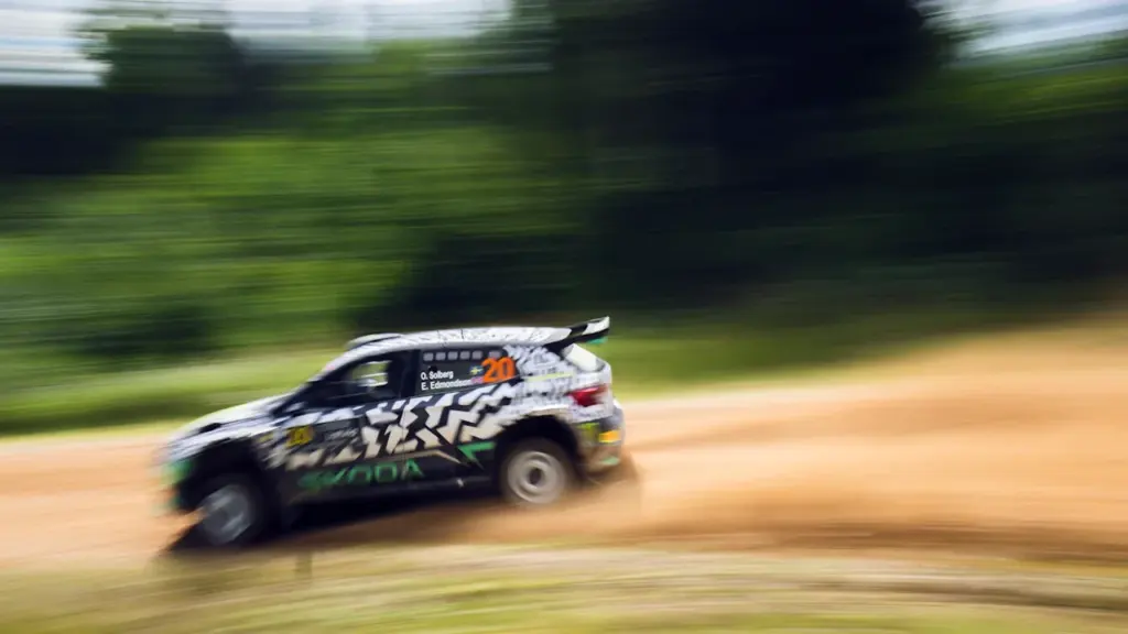 Sporta rallija automašīna ātri brauc pa grants ceļu meža ielokā Latvijā